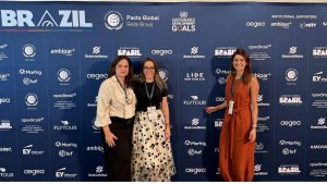 Manuela Bernardes ao lado esquerdo, Renata Maluf ao lado direito e Andrea Panisset no centro. Painel azul do SDGs na ONU em Nova Iorque. Flytour participa do SDGs in Brazil 2024, destacando seu compromisso com ESG e o Pacto Global. Conheça as ações de sustentabilidade no turismo corporativo.